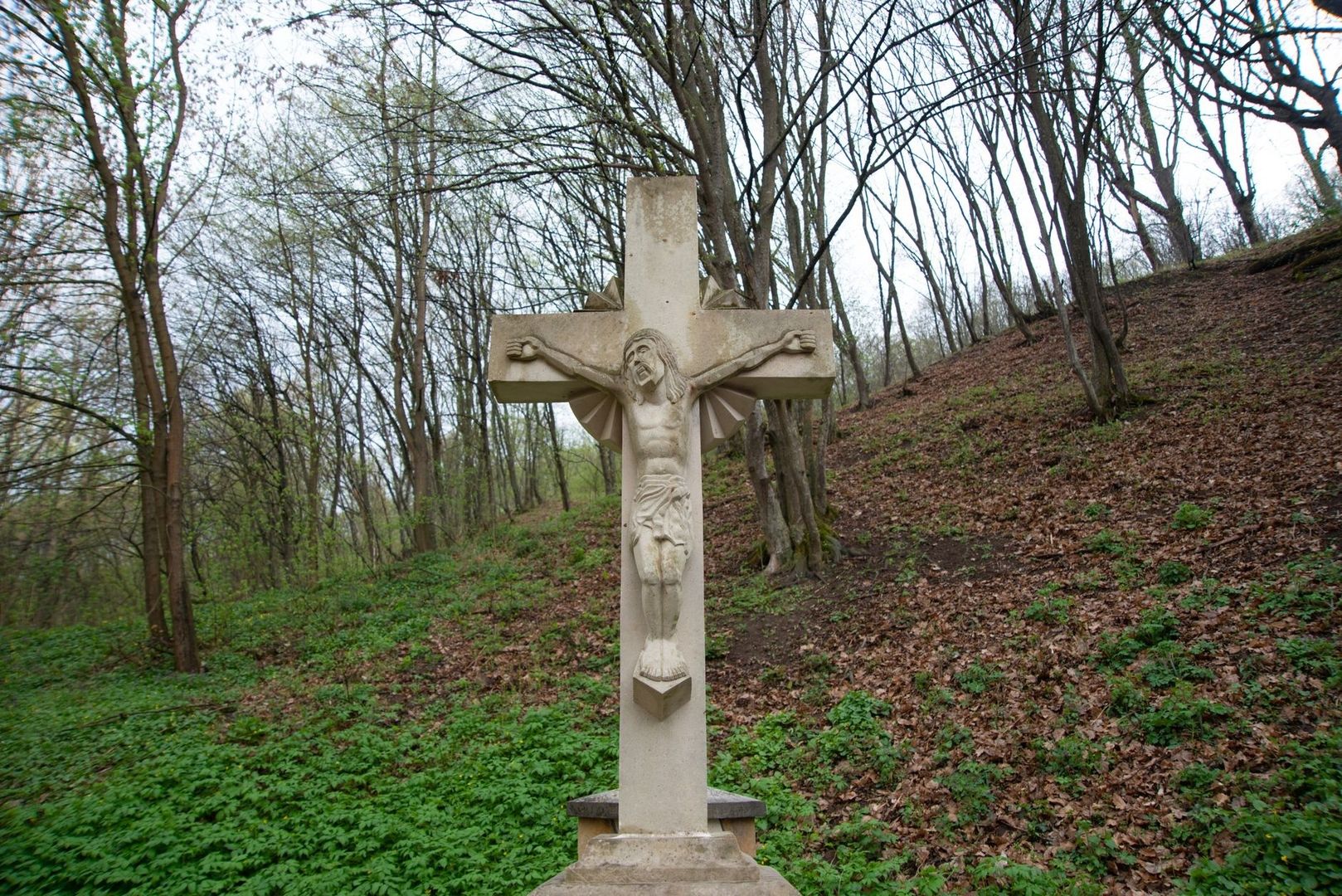 Stenkors med Jesusfigur i en stilla, lövklädd skogssluttning